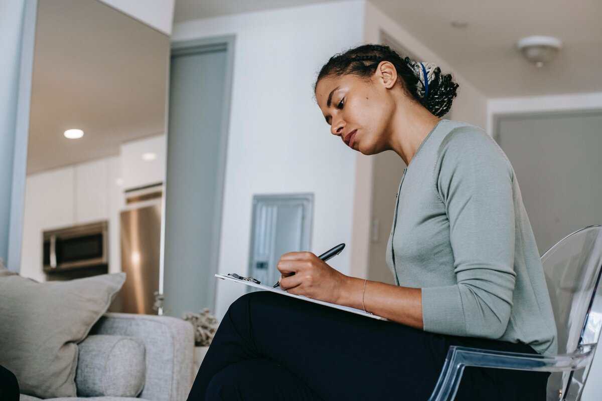 A person sitting on a couch and writing on a clipboard.