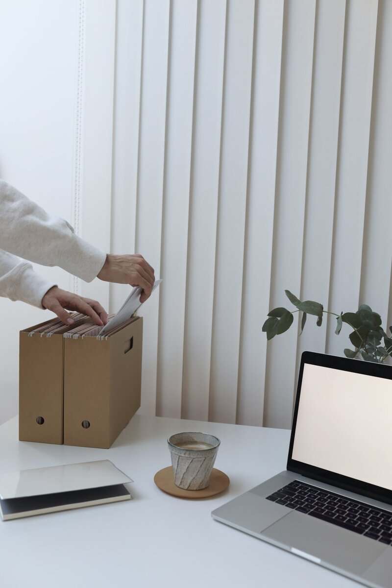 A person placing a paper into a filing box on a computer desk.