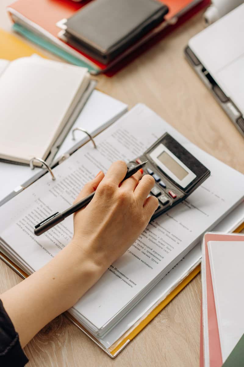 A person using a calculator and writing on a spread sheet.