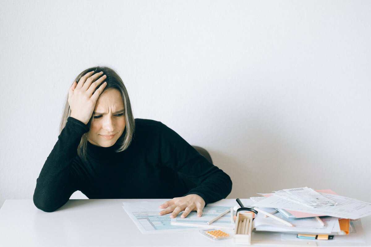 A person at a desk, destressed and looking a paperwork.