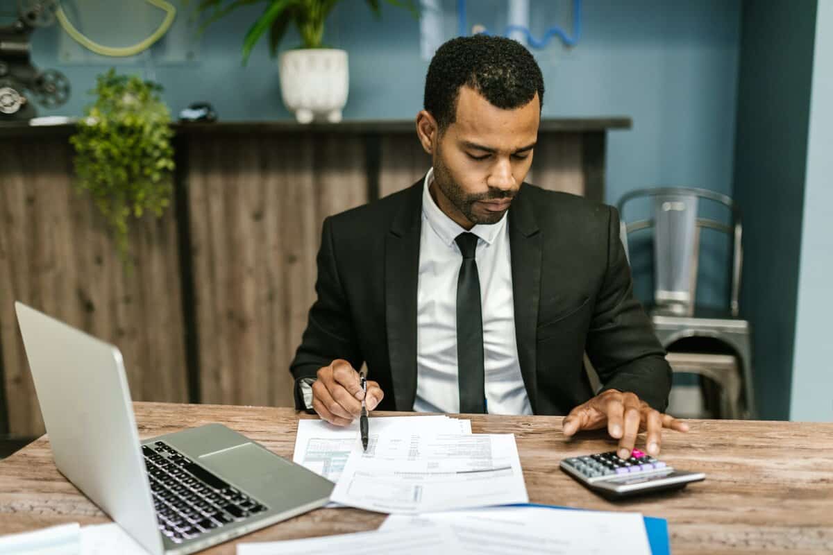 A person sitting at a desk reviewing paperwork and using a calculator.