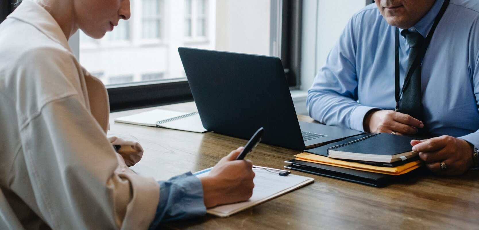 A person at a computer across from a person with a clipboard.