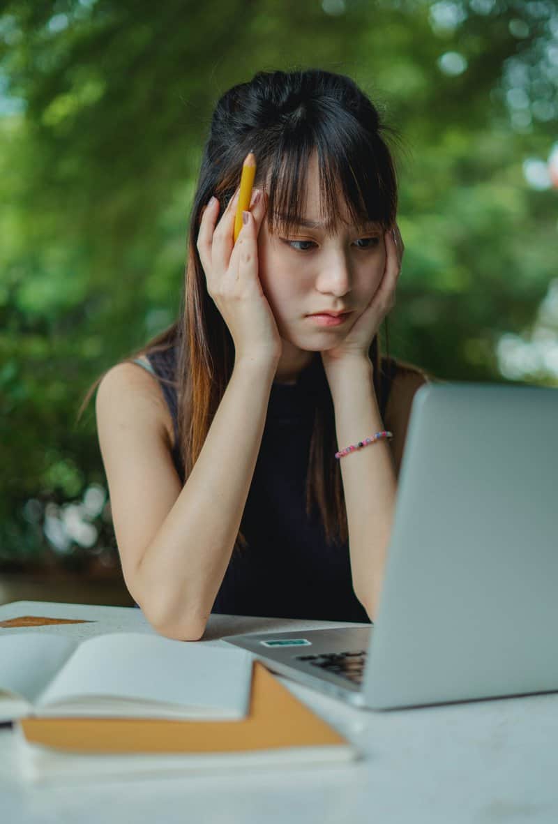 A person at a desk holding their head up, looking at a computer screen.